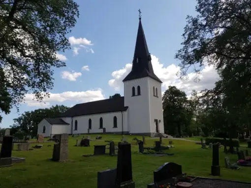 Baksidan av Hjälstads kyrka med gravvårdar och grönska i kyrkomiljön.