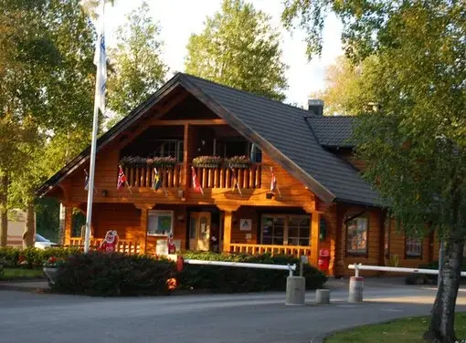 En timrad huvudbyggnad med flaggor och välkomnande entré på Billingens Stugby & Camping.