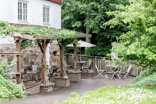 En charmig uteservering med träpergola täckt av grönska, bord och stolar omgivna av natur vid Herrtorps Qvarn & Öringen.