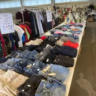 Kläder till salu på JMN Loppis och Café Ett långt bord med olika klädesplagg som jeans, skjortor och toppar på JMN Loppis och Café.