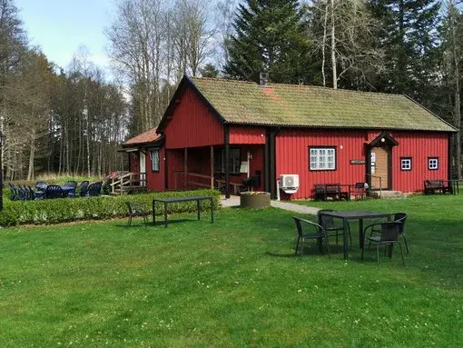 Kaffestugan i Alphems Arboretum - Historisk charm Kaffestugans röda byggnad omgiven av grönska och uteservering med sittplatser.
