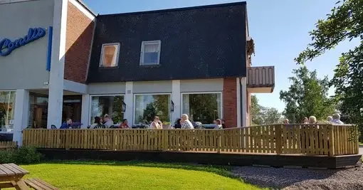 Uteservering med bord och stolar framför konditoriet i solskenet.