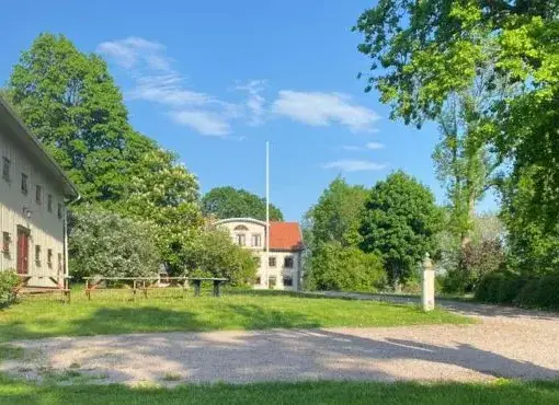 Utsikt över huvudbyggnaden på Sjötorps Säteri, omgiven av lummiga träd och grönska.