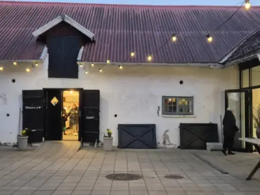 Ingången till Vilhelmsro Gårdscafé med öppna dörrar, varm belysning och folk i rörelse under kvällstid.