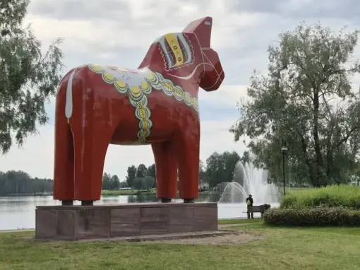 Näst största dalahästen i världen står vid vattnet i Mora, med fontän och träd i bakgrunden.