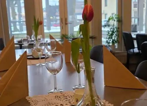 Långbord dukat med vikta servetter, vinglas och tulpan i vas i ljus restaurangmiljö hos Hildes Matglädje i Falköping.