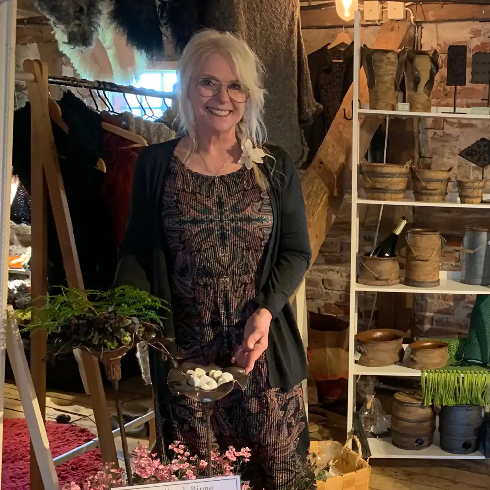 Marina Bonnevier står i sin butik omgiven av keramik och hantverk, håller ett keramikföremål i händerna.