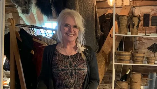 Marina Bonnevier står i sin butik omgiven av keramik och hantverk, håller ett keramikföremål i händerna.