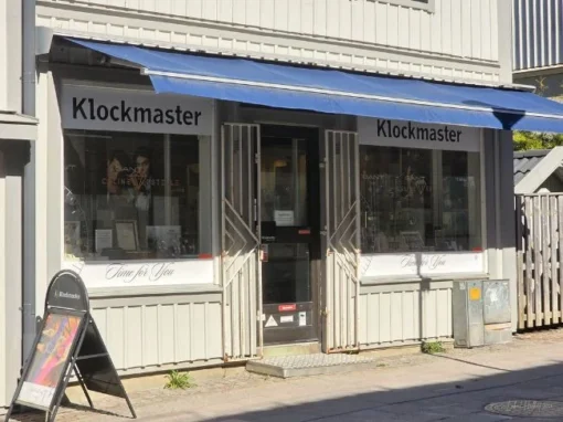 Klockmaster i Falköping med butiksfasad, skyltfönster, blå markis och entré längs gatan.