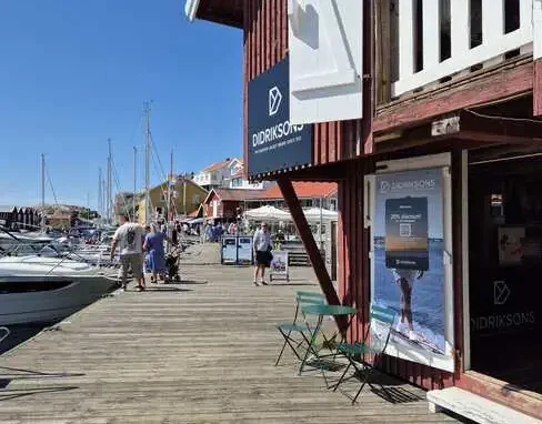 Butiker och båtliv längs Smögenbryggan Träbrygga med butik i sjöbod, båtar och besökare längs Smögenbryggan.