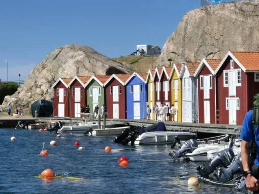 Färgstarka sjöbodar i rött, blått, grönt och gult längs Smögenbryggan med båtar i hamnen.